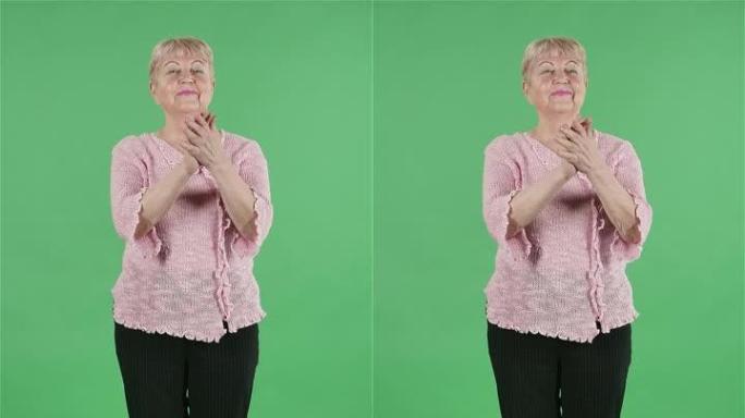 肖像老年妇女看着相机微笑着拍手。在工作室的绿色屏幕上，白发祖母，短发穿着粉红色的毛衣。慢动作。垂直视