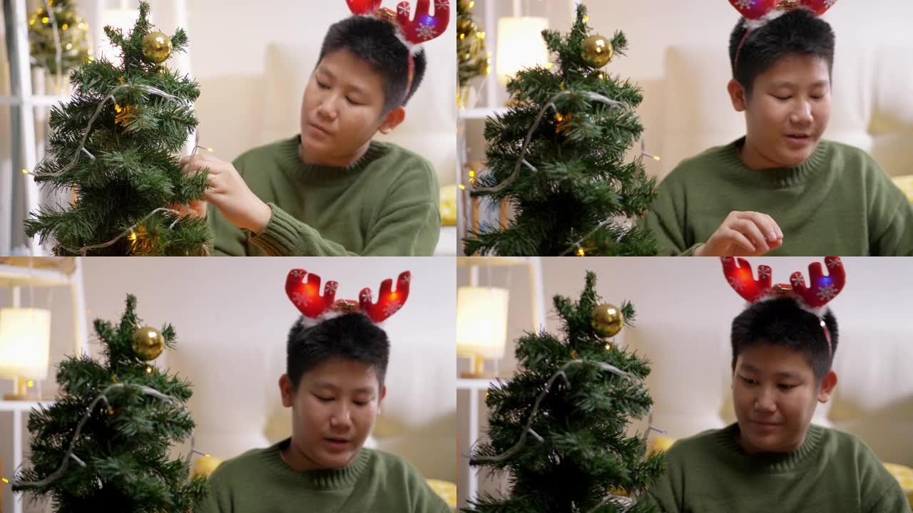 快乐的亚洲男孩穿着绿色毛衣和红色发带装饰圣诞树，晚上在家，假期概念。