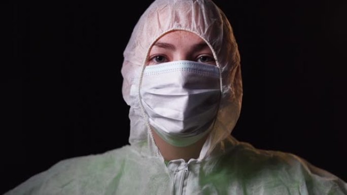 年轻女医生的肖像照片，穿着白色防护服，脸上戴着黑色背景的医用口罩。冷静地站着，看着镜头