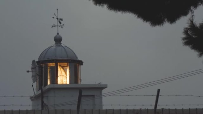 灯塔发出的光束透过雨滴闪耀。海边的恶劣天气