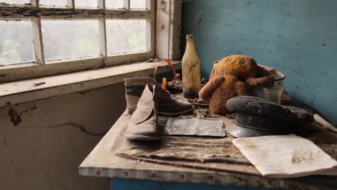 乌克兰切尔诺贝利区。参观普里皮亚季鬼城-4K.桌子、靴子、毛绒玩具、帽子在旧窗户旁边的桌子上