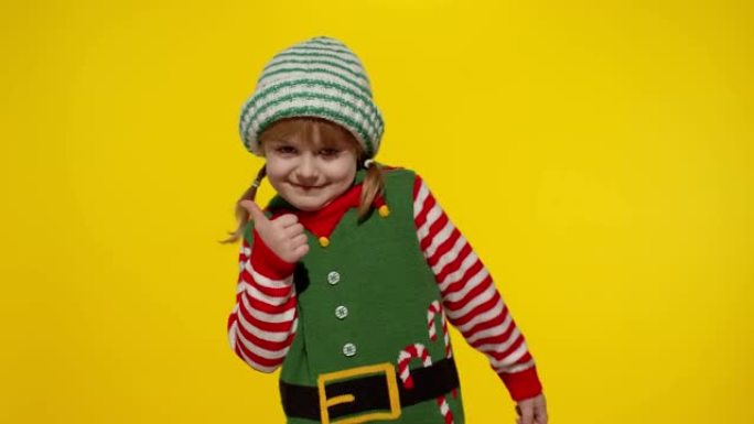 穿着圣诞精灵圣诞老人帮手服装的小女孩孩子表现出竖起大拇指的姿态。新年假期