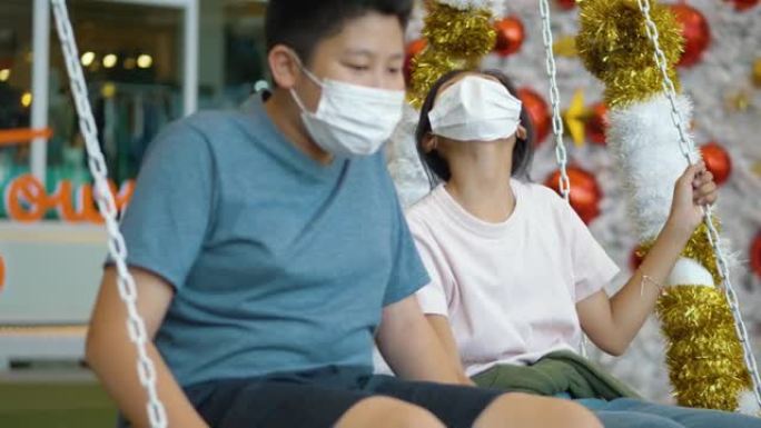 快乐的亚洲儿童戴着口罩，用圣诞树背景拍照或自拍，假期概念。