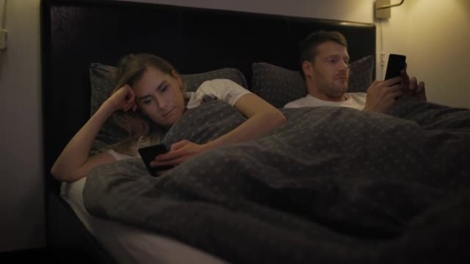 已婚夫妇在床上使用智能手机，彼此无视。关系常规沟通问题网络成瘾概念