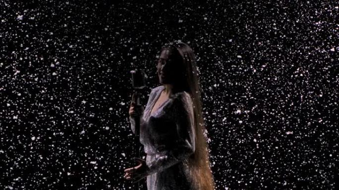 美丽的歌手的剪影，带有老式麦克风，背景是飘落的雪。穿着闪亮连衣裙的年轻女子在一个空旷的舞台上对着麦克