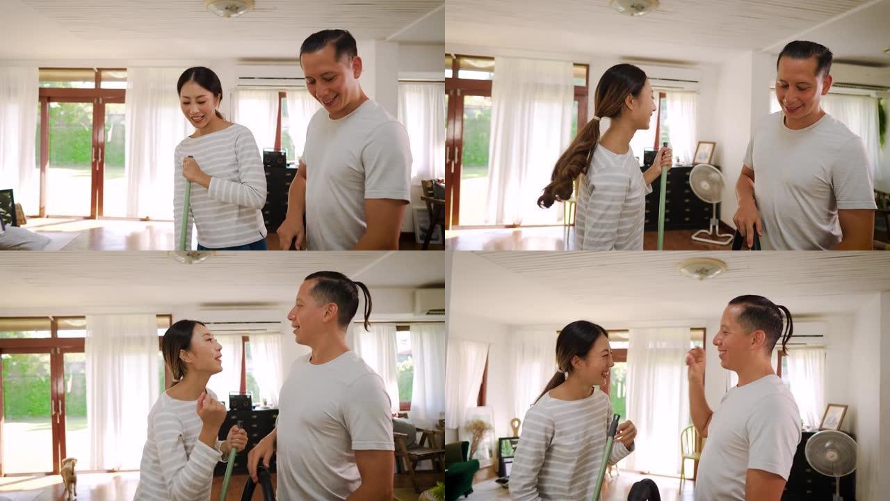 幸福的年轻夫妇在用吸尘器清洁时跳舞和唱歌，男人在现代家庭的客厅拖地