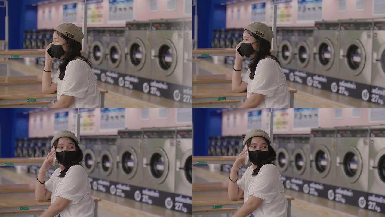 亚洲女孩手里拿着智能手机时戴着maskat。她在自动洗衣店打电话。