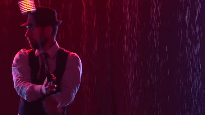 马戏团艺术家用发光的手榴弹表演技巧。时尚的男人站在雨中，以红灯为背景。戴帽子的艺术家剪影特写。慢动作