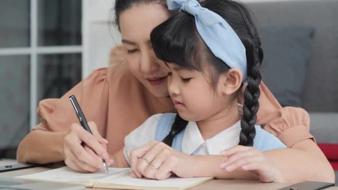 亚洲妈妈牵着女儿的手写书学习。用心学习。