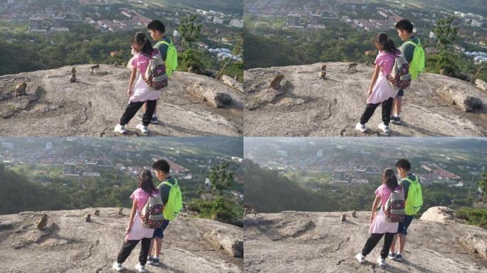 快乐的亚洲背包客儿童用智能手机，生活方式概念在山顶上拍摄猴子的照片。