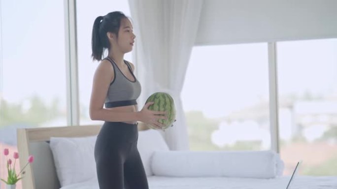 年轻的亚洲妇女在卧室在线教程的帮助下在家用西瓜锻炼