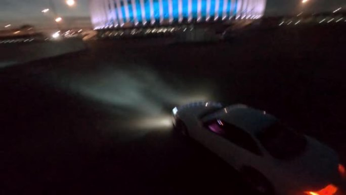 白色跑车在现代照明建筑附近的空停车场上漂移，夜间对着黑暗城市第一视点电影空中跟随fpv赛车快速无人机