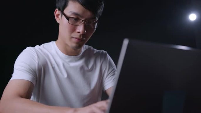 关闭亚洲男程序员在笔记本电脑夜间工作到很晚，专注于工作室拍摄黑暗背景