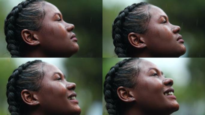 阵雨中的黑人女孩。特写镜头非洲年轻女子在下雨时带着希望仰望天空
