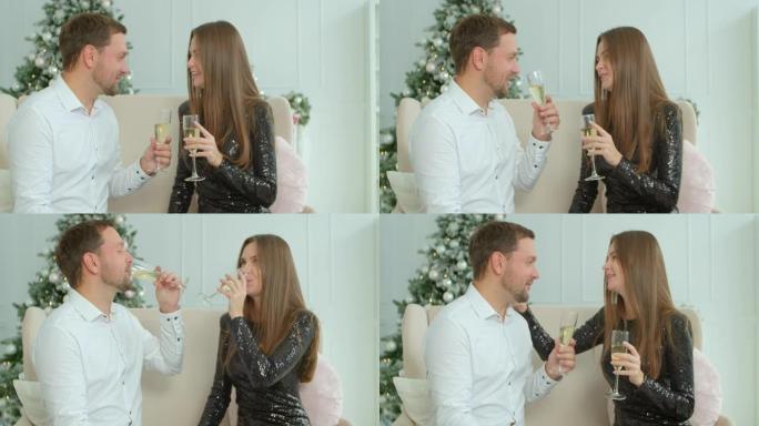 一对夫妇坐在发光的枞树附近的沙发上，拿着香槟杯说祝酒，祝大家一起庆祝圣诞节。圣诞夜在现代装饰的房子里