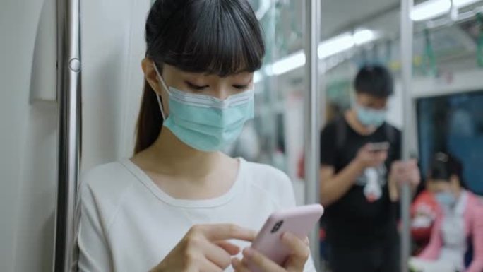亚洲女性戴着口罩，使用智能手机和耳机，在地铁或火车上通勤时保持社交距离