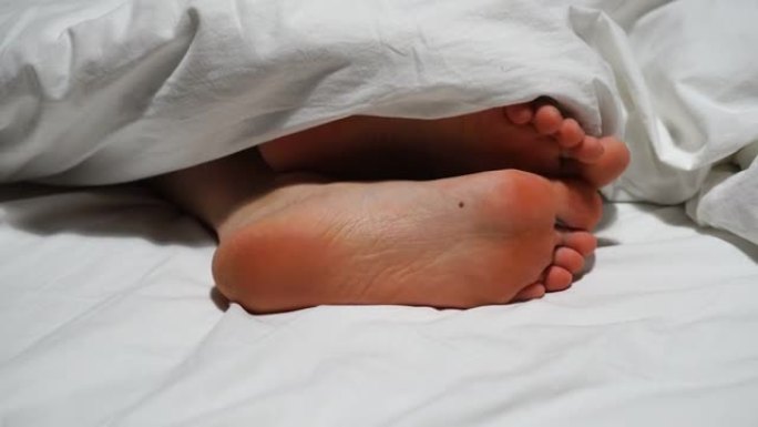 女人的脚踩在白色的床上，盖着白色的毯子