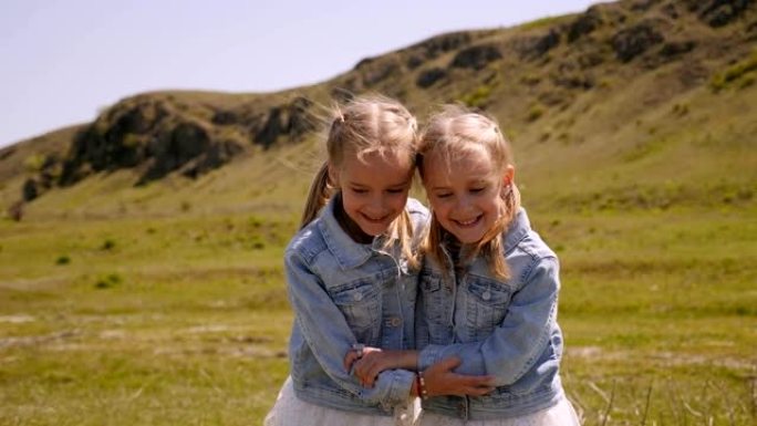 在阳光明媚的山脉背景下的田野中，双胞胎姐妹的肖像