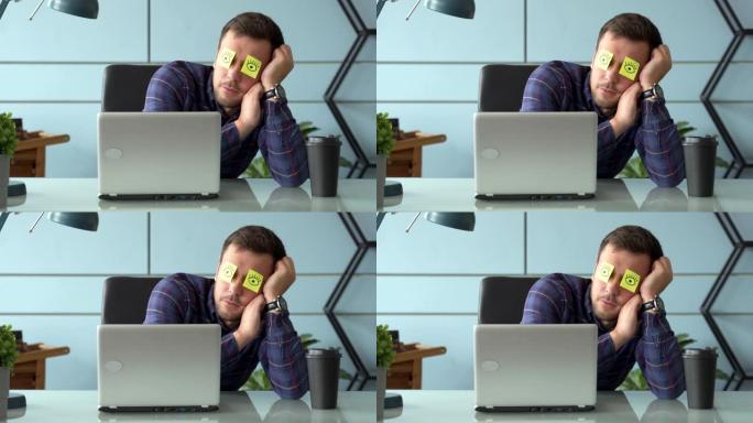 疲惫的漫画男经理假装工作时脸上贴着贴纸坐在笔记本电脑的桌子上睡觉