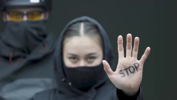 抗议的女性示威者用手做停止手势。带着黑色面具的激进分子的女人在纠察