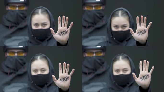 抗议的女性示威者用手做停止手势。带着黑色面具的激进分子的女人在纠察