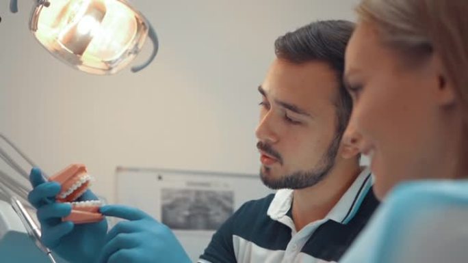 男性牙医向患者展示了带有牙套的颌骨人工模型。如何正确护理您的口腔，戴上牙套，成本和后果