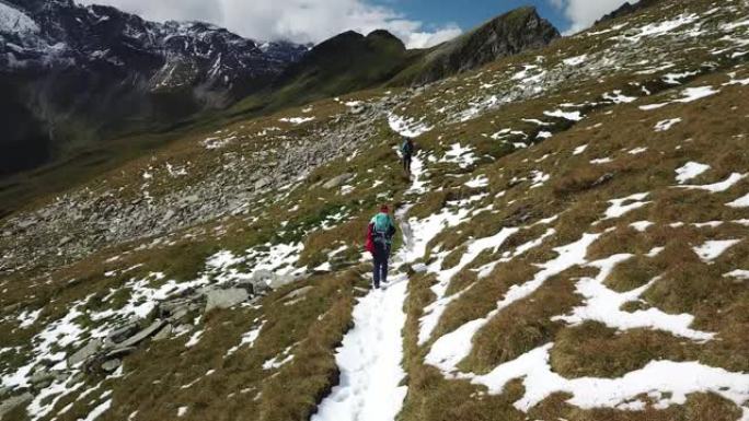 一对带着大背包的夫妇在奥地利的Hohe Tauern地区徒步旅行。斜坡部分被雪覆盖。上部陡峭而锋利。