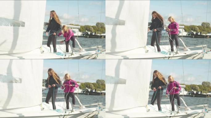 两个可爱的女孩站在一艘白色游艇的船尾，拉着绳索控制帆