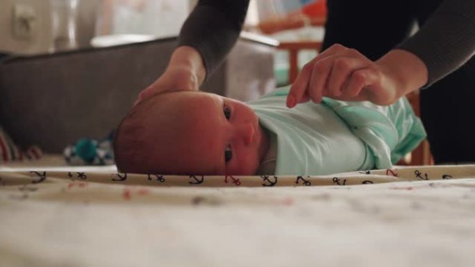 母亲襁褓着她刚出生的婴儿。把婴儿用尿布包起来。新生儿躺在床上