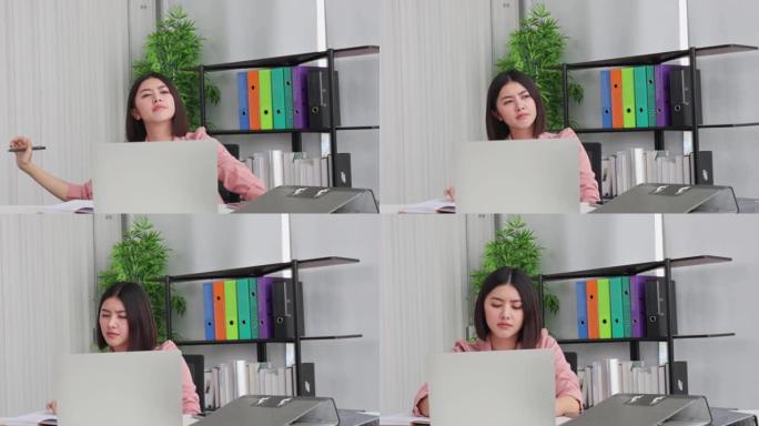 亚洲自由职业女性在办公室客厅工作时在笔记本电脑上工作。女孩坐在办公桌上加班，享受放松时间。女性工作压