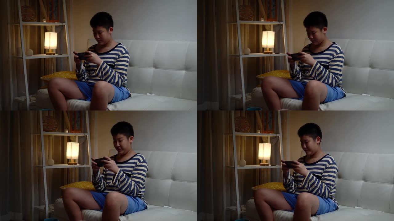 快乐的亚洲男孩在家坐在沙发上玩手机网络游戏，生活方式理念。