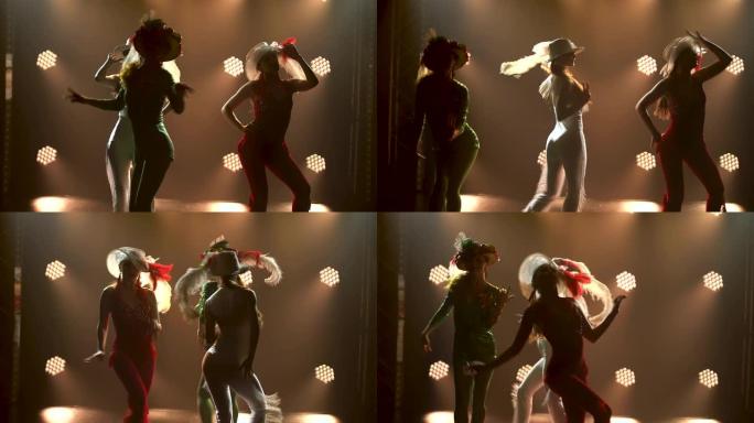 三个美丽的年轻女子穿着绿色、白色和红色闪亮的紧身西装和原创帽子跳舞和摆姿势的剪影。戏剧女性舞蹈表演。
