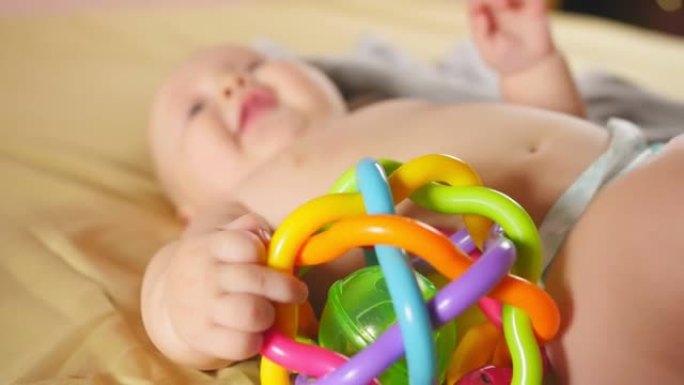 四个月的婴儿在离焦的床上玩拨浪鼓。婴儿拨浪鼓的特写镜头。儿童的感觉发育。特写镜头。