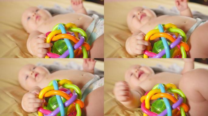 四个月的婴儿在离焦的床上玩拨浪鼓。婴儿拨浪鼓的特写镜头。儿童的感觉发育。特写镜头。