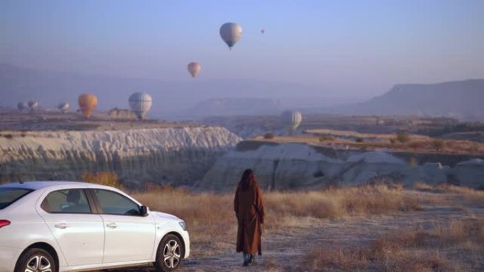 在土耳其卡帕多西亚的汽车旁看着热气球的女人