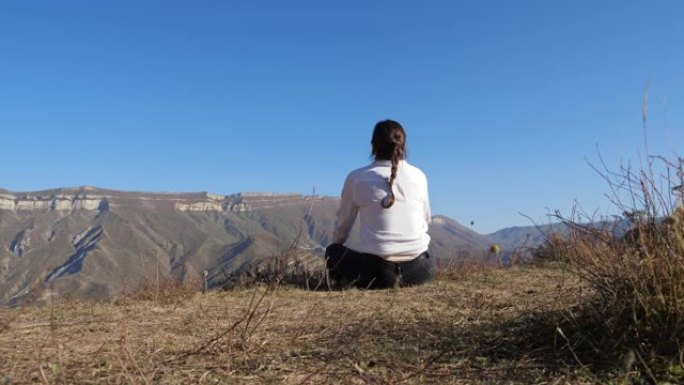 穿着白衬衫的黑发女人坐在山上晴朗的天空下的地面上