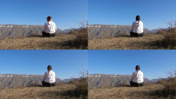 穿着白衬衫的黑发女人坐在山上晴朗的天空下的地面上