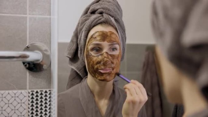 女人在浴室的镜子前用刷子涂泥面膜。护肤美容护理