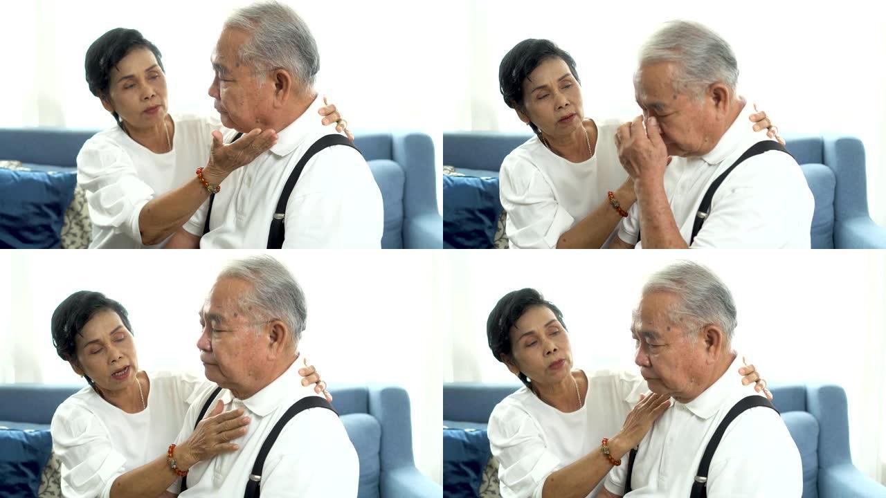不幸的退休亚洲老年夫妇坐在沙发上，年迈的妻子在家安慰悲伤的丈夫。