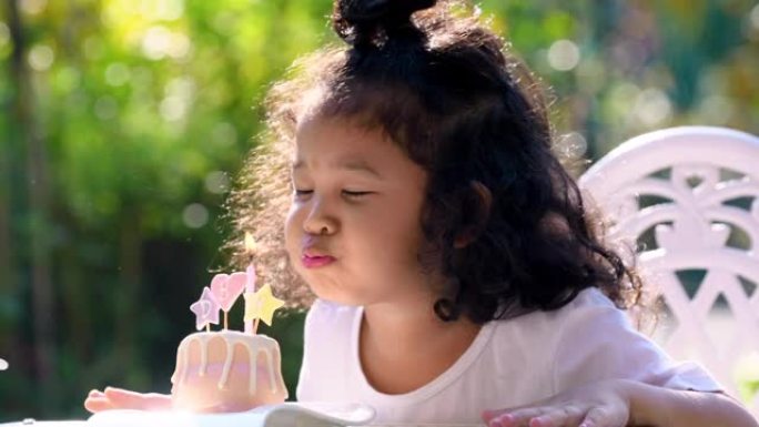 亚洲家庭生日派对快乐。可爱的小女孩的特写镜头用笑脸在小生日蛋糕上吹灭蜡烛。快乐小可爱女儿在家和爸爸妈
