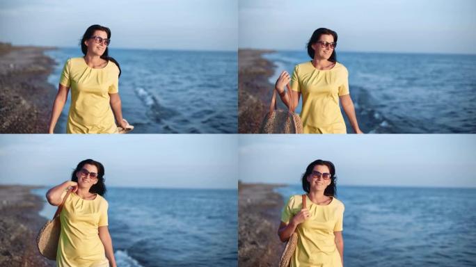 优雅快乐的女人戴着墨镜，穿着黄色的衣服走在日落的海滩上。4k Dragon RED摄像机