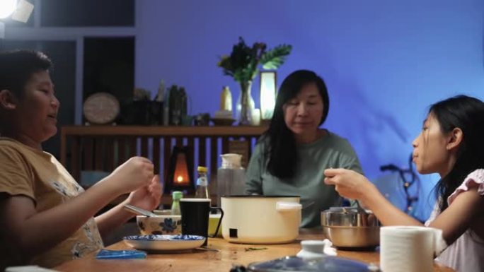 快乐的亚洲单身母亲和她的孩子一起欢呼喝酒，一边在家吃晚餐，带led灯背景，生活理念。