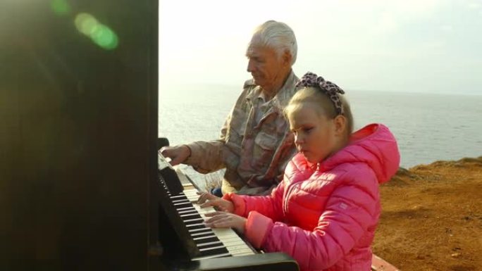 老人和小女孩在海岸上一起弹钢琴