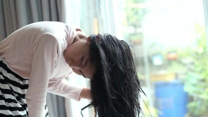 亚洲女孩在家里用吹风机为她潮湿的头发靠近窗户，生活方式的概念。