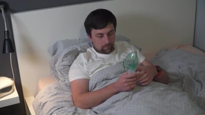 男子冠状病毒，流感使用压缩机雾化器药物吸入器面罩在床上。呼吸内科。哮喘呼吸治疗。支气管炎，哮喘保健设