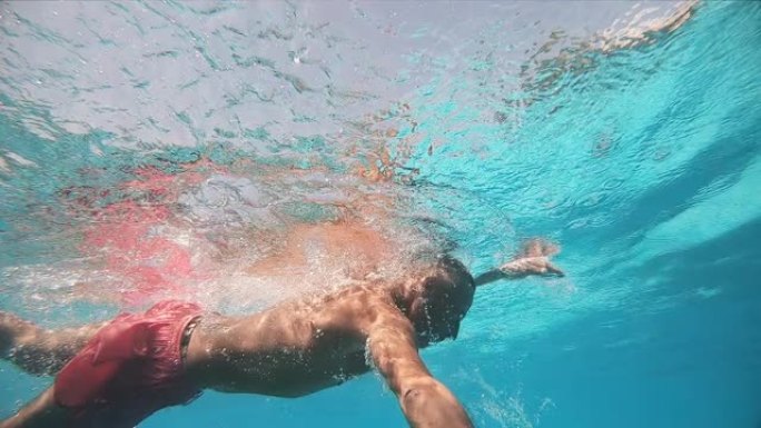 男子在游泳池里游泳爬行。水下慢动作视图