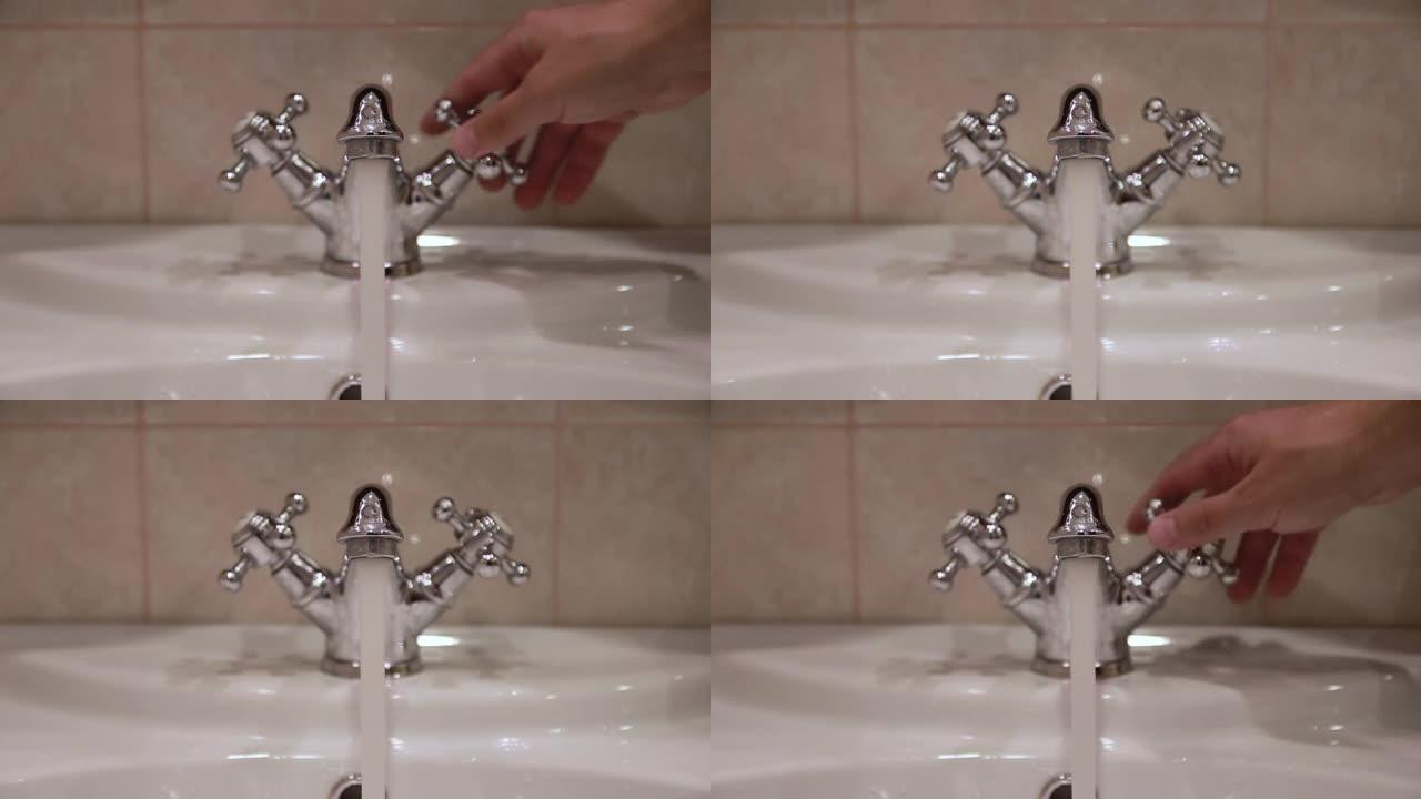 用手打开浴室洗脸盆里的水龙头。