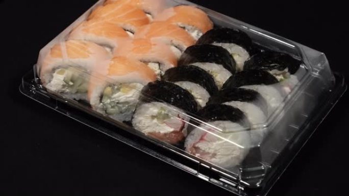 寿司卷在黑色背景上的塑料容器中旋转。送餐