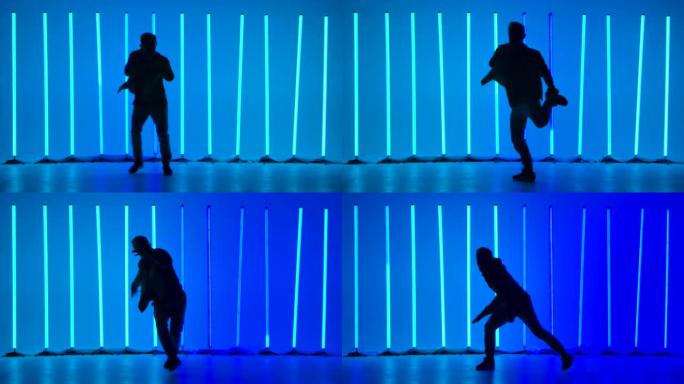 一个穿着时尚青年服装的年轻人的剪影在黑暗的工作室里明亮的蓝色霓虹灯的背景下跳霹雳舞街舞。慢动作