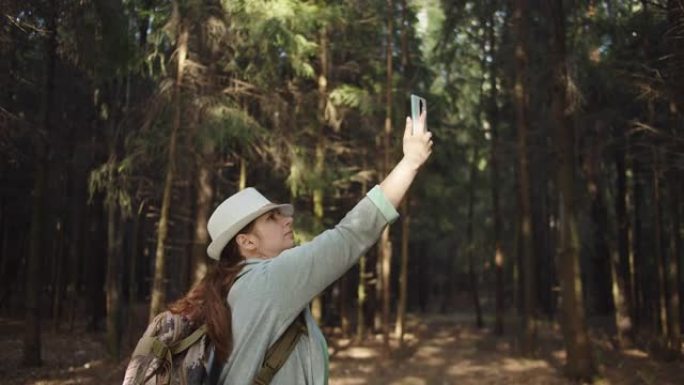 戴着帽子的旅行者女人试图在森林里的手机上捕捉手机信号，但手机上没有信号